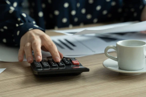 Close up woman planning budget, using calculator and laptop, reading documents, sitting at desk