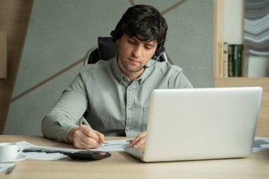 Kulaklıklı ve dizüstü bilgisayarlı bir adam ofiste video konferansı yapıyor. İş yerinde konuşan ve el kol hareketi yapan bir erkek bir video konferansı düzenliyor.