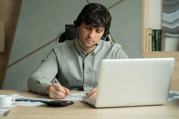 Hombre con auriculares y computadora portátil que tiene videoconferencia en la oficina. Hombre en el lugar de trabajo, hablando y haciendo gestos, está celebrando una videoconferencia — Foto de Stock