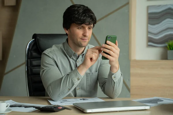 Мужчина в рубашке сидит в офисе и использует смартфон для работы — стоковое фото