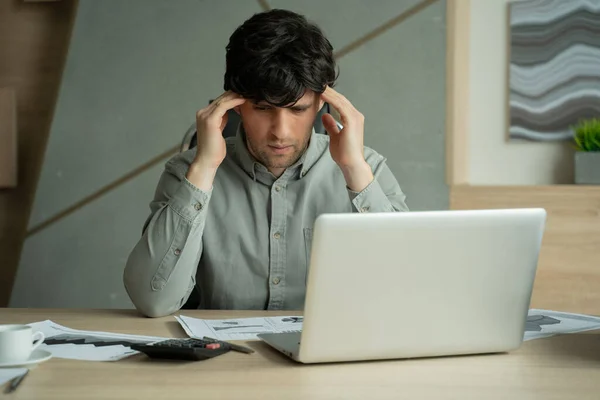Απογοητευμένος άνθρωπος, ενώ κάθεται στο χώρο εργασίας του στο γραφείο. Εξαντλημένος νεαρός με φορητό υπολογιστή στο γραφείο — Φωτογραφία Αρχείου