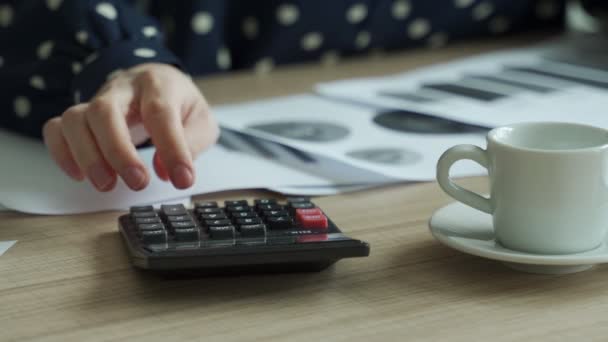 Закрыть бюджет женского планирования, используя калькулятор и ноутбук, читая документы, сидя за столом — стоковое видео