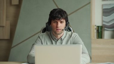 Kulaklıklı ve dizüstü bilgisayarlı bir adam ofiste video konferansı yapıyor. İş yerinde konuşan ve el kol hareketi yapan bir erkek bir video konferansı düzenliyor.