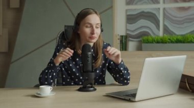 Mikrofonu ve dizüstü bilgisayarı olan bir kadın stüdyoda konuşuyor ve podcast yapıyor.