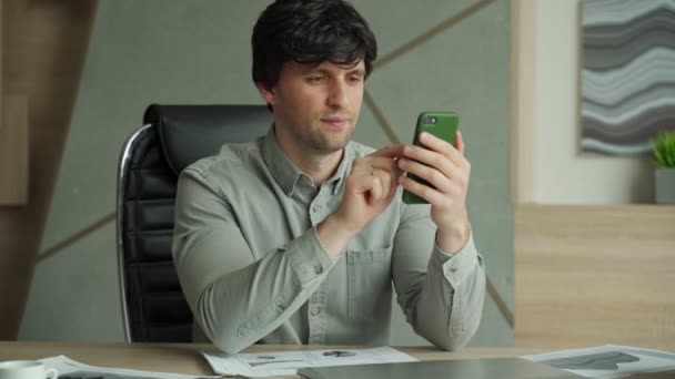 Affärsman som använder smartphone sitter på kontoret, har goda nyheter på telefon — Stockvideo