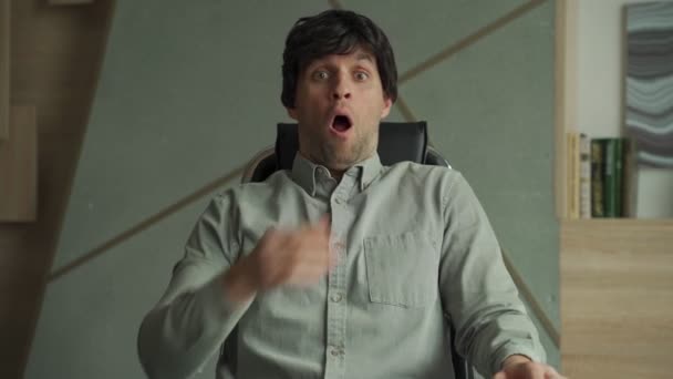 Jeune homme avec une expression surprise est assis dans une chaise dans le bureau — Video