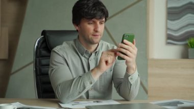 Ofiste oturan ve iş için akıllı telefon kullanan gömlekli bir adam.