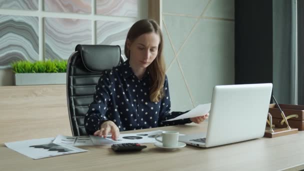 Donna d'affari in camicia casual lavora presso una scrivania bianca con un computer portatile, buttando documenti contabili cartacei — Video Stock