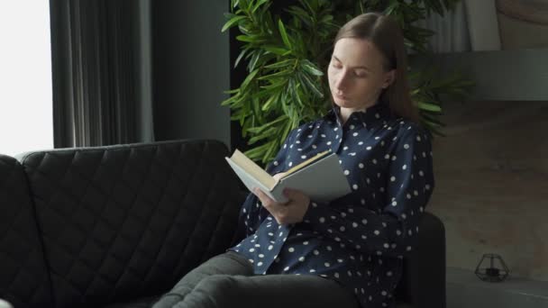 Een jonge vrouw die thuis een sprookjesboek leest op de bank. Vrouw die thuis boek leest. — Stockvideo