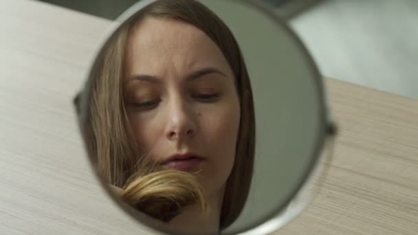 Mulher olha para o reflexo de um espelho redondo, vê cabelos secos, sem vida, danificados e emaranhados — Vídeo de Stock