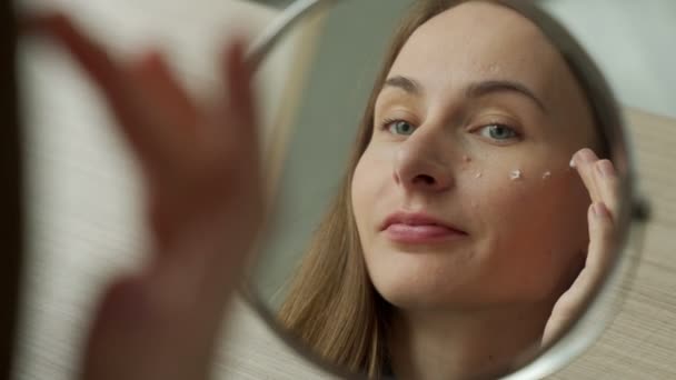 Frau tragen Gesichtscreme Look im Spiegel auf. Weibliche Anwendung von Gesichtscreme während der Morgenroutine — Stockvideo