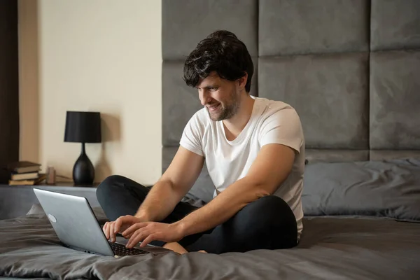 Взволнованный мужчина, сидящий на кровати с ноутбуком, празднует успех — стоковое фото