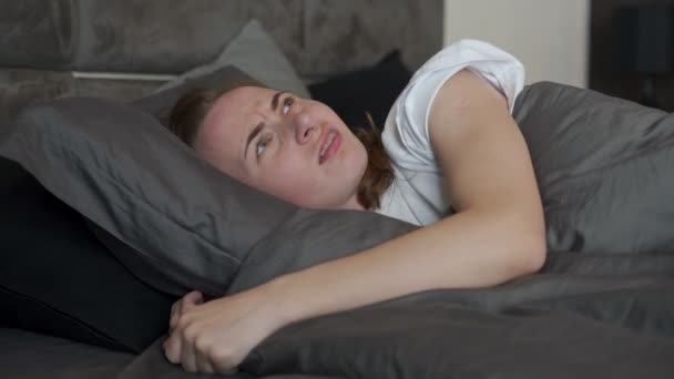 Tired woman cant sleep. A sleepless woman covers her ears with a pillow. I wake up in bed in the middle of the night because of noisy neighbors — Stock Video