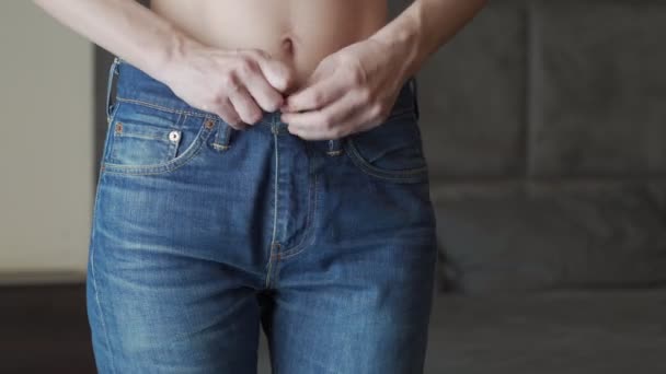 Молодая спортсменка надевает джинсы и они становятся большими для нее, показывает ее плоский желудок, быстро похудел — стоковое видео