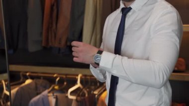 Soyunma odasında kol saatini ilikleyen tişörtlü bir adam var.