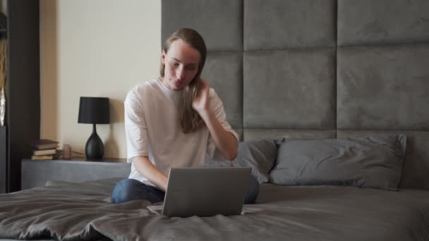 Mujer joven gana y celebra los gritos con el ordenador portátil mientras está sentado en la cama en casa — Vídeo de stock