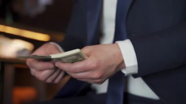 Yakın plan işadamı giyim mağazasında bir sandalyede otururken Amerikan doları sayıyor.