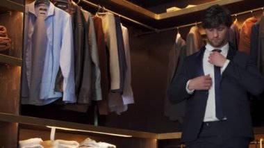 Dükkanda ceket deneyen zarif bir adam. Arka planda klasik takım elbiseler ve ceketler