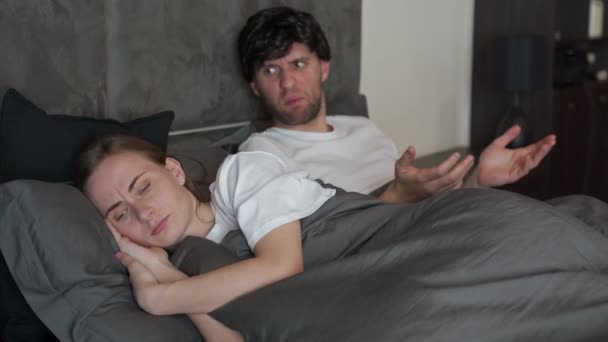 Jonge boze trieste geïrriteerde man schreeuwt tegen een vrouw die binnen op een bed zit in de slaapkamer van een huis — Stockvideo