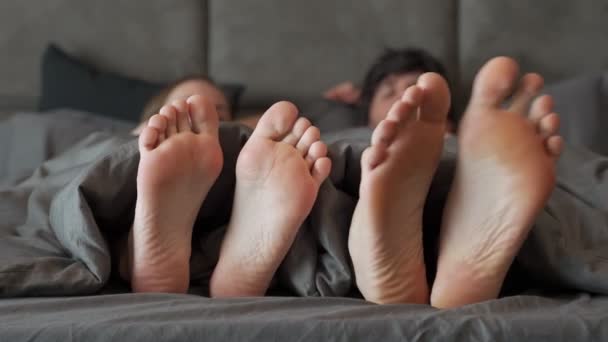 Любляча радісна пара грає і танцює ноги під ковдрою, прокидаючись в ліжку вранці — стокове відео