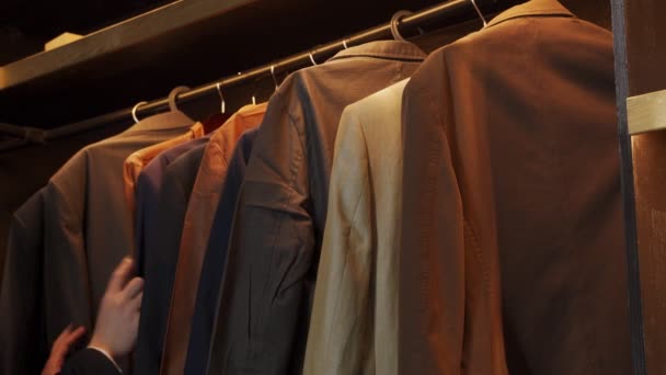Primer plano hombre elige trajes en una percha en una tienda de ropa para hombres — Vídeo de stock