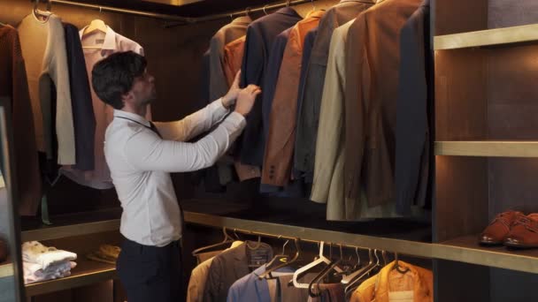 Мужчина выбирает деловую куртку, висящую на вешалках в магазине одежды. — стоковое видео