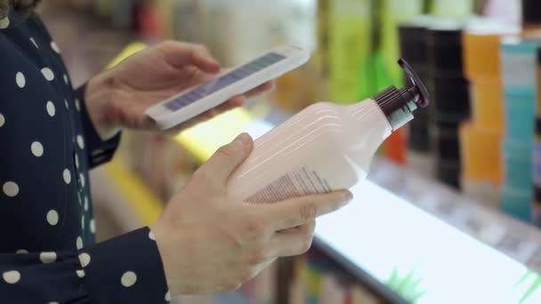 Close-up af en kvindelig handske hænder scanner sammensætningen af en kropscreme med en smartphone i butikken – Stock-video