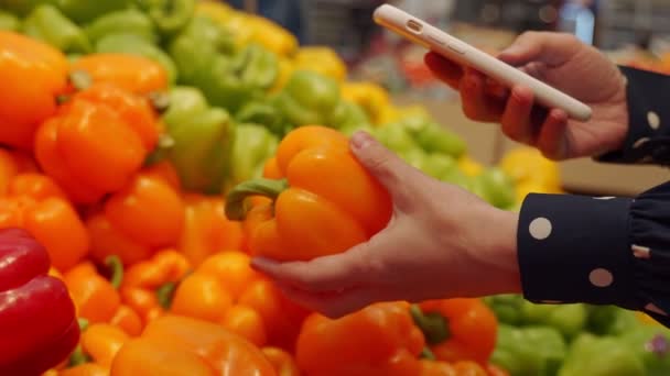 Woman chooses an orange bell pepper in a grocery store, at the market. — Stock Video