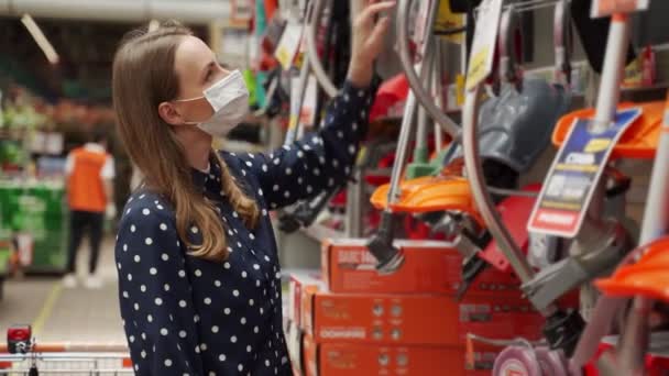 Young woman in a medical mask came to the garden tools store to buy a lawn mower — Stock Video