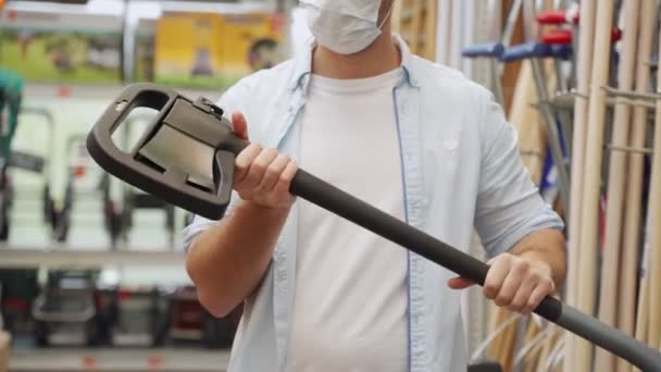 Hombre con máscara médica recoge un hacha en el departamento de construcción de un centro comercial — Vídeo de stock