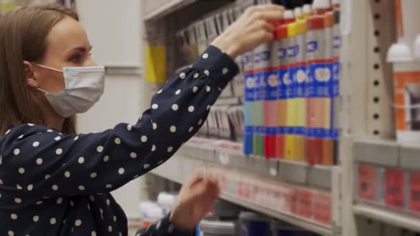 Mujer con máscara protectora elige pintura en una ferretería — Vídeo de stock