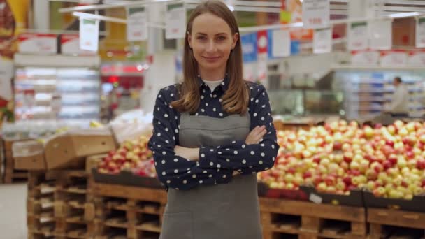 Retrato de uma trabalhadora em um avental, contra um fundo de frutas, uma jovem cruza os braços em uma mercearia e olha para a câmera — Vídeo de Stock