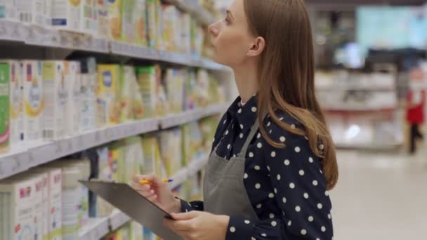 Kobieta w fartuchu pracująca w supermarkecie. Kobieta pisze na tablecie, by spisać produkty w witrynie sklepu spożywczego.. — Wideo stockowe