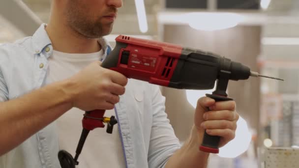 Человек в защитной маске выбирает электрическую дрель в магазине инструментов — стоковое видео