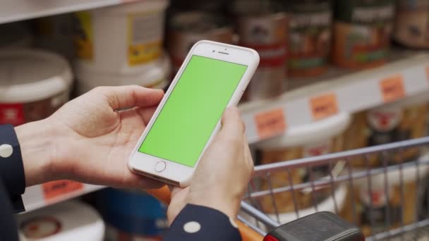 Mujer utiliza un smartphone con pantalla verde en una ferretería — Vídeo de stock