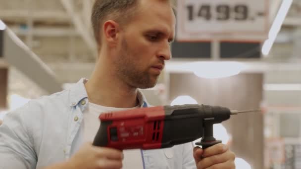 Homme dans un masque de protection choisit une perceuse électrique dans un magasin d'outils — Video