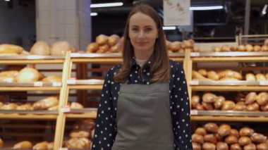 Şekerci dükkanında önlüğüyle küçük bir pastanesi olan bir kadın. Bir kadın ekmeğin arkasındaki kameraya bakar.