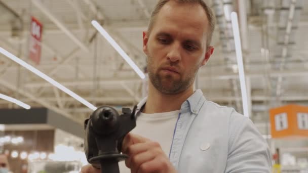 Mann mit Schutzmaske greift im Werkzeugladen zur Elektrobohrmaschine — Stockvideo