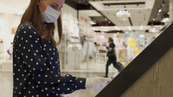 Kvinnan bär en skyddande mask och handskar vidrör den känsliga skärmen på en interaktiv informationskiosk med fingrarna — Stockvideo