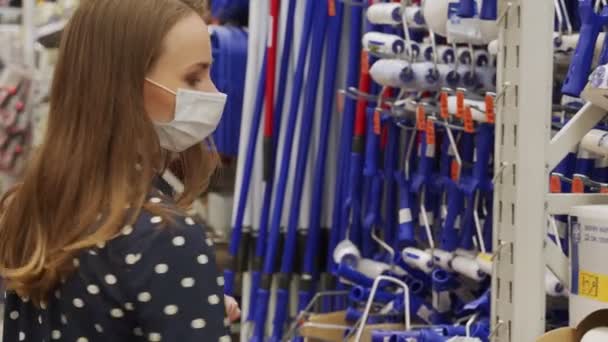 保護マスクの女性は、ハードウェアストアで新しいペイントローラーを選択します — ストック動画