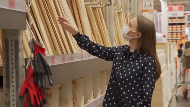 Žena s ochrannou maskou v obchodě vybírá dřevo pro tesařské práce. — Stock video