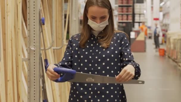 Donna che indossa una maschera protettiva nel negozio di costruzione sceglie sega a mano. — Video Stock