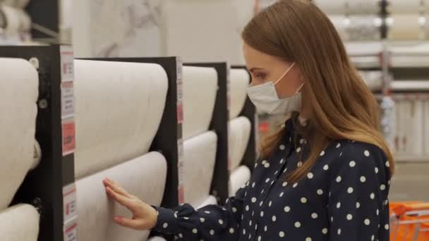 Vrouw met een beschermend masker kiest behang in een ijzerwinkel. Het concept van reparaties en aankopen. — Stockvideo