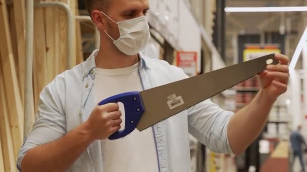 Muž v ochranné masce zvedne ruční pilu v železářství — Stock video