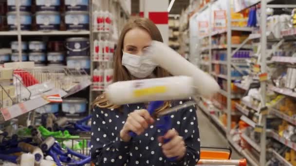 Koruyucu maskeli genç bir kadın hırdavatçıda boya silindirleri tutuyor. — Stok video