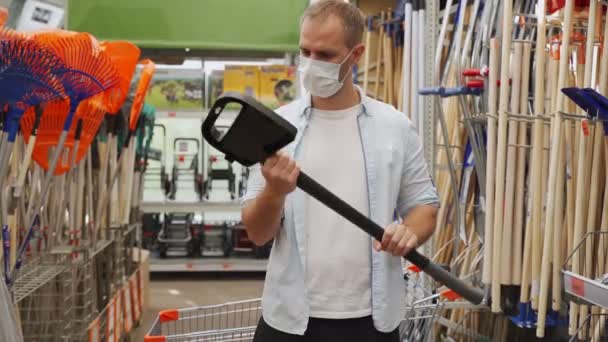 Muž v lékařské masce zvedne sekeru na stavebním oddělení nákupního centra — Stock video