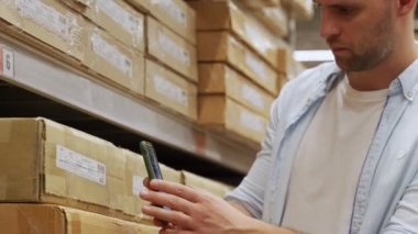 Adam akıllı telefonuyla depodaki kutuları tarıyor..