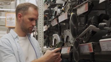 Adam bir alet dükkanında akıllı telefon kullanarak dairesel bir testere seçiyor. Erkek bir hırdavatçıdan ürün seçer..