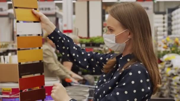 Nainen suojelevassa naamiossa valitsee maalin värin puulle rautakaupassa — kuvapankkivideo