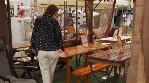 Женщина в медицинской маске выбирает стол в мебельном магазине — стоковое видео